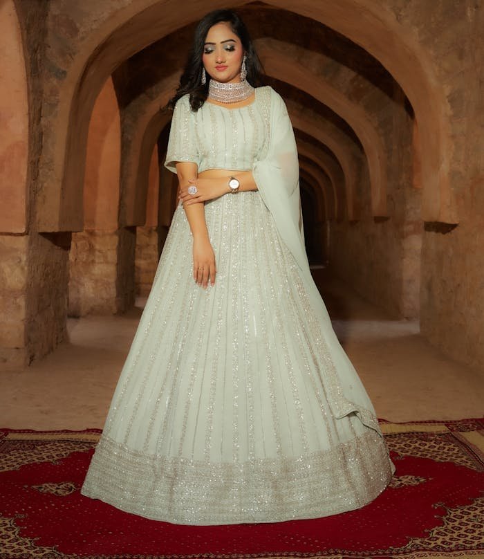 A beautifully dressed woman stands gracefully in an ancient architectural corridor.